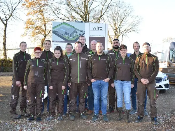 Eine Gruppe von Mitarbeitenden eines Handwerksbetriebs steht vor einem Firmenschild im Freien.