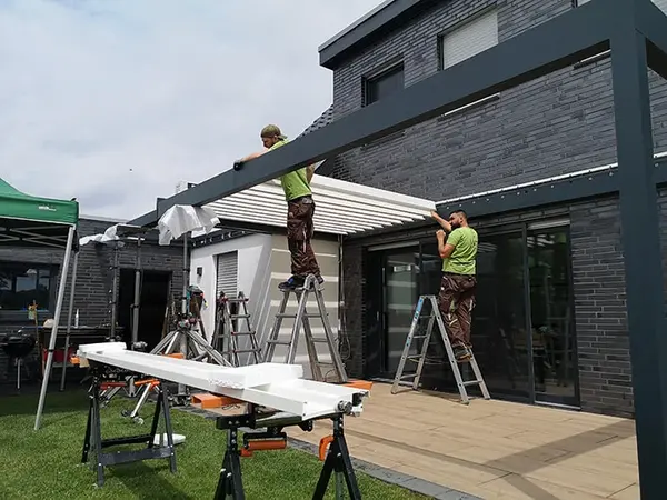 Zwei Handwerker montieren eine moderne Terrassenüberdachung an einem Einfamilienhaus.