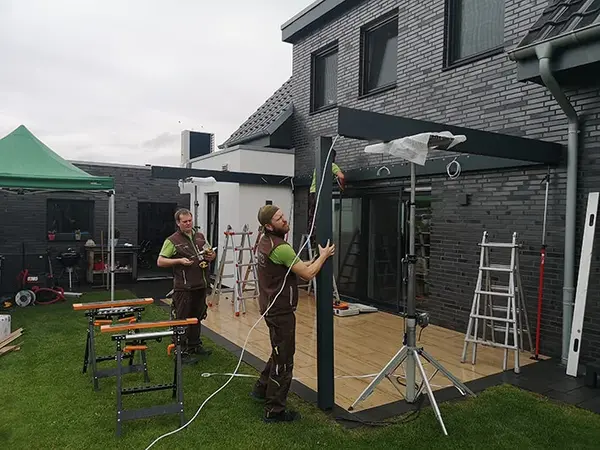 Handwerker montieren eine moderne Terrassenüberdachung an einem Einfamilienhaus aus Klinker.