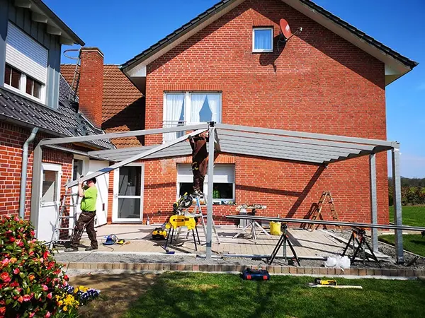 Handwerker bauen eine moderne Terrassenüberdachung an einem Einfamilienhaus aus Klinker.