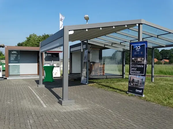 Moderne Überdachung auf Ausstellungsfläche mit Glasdach und Outdoor-Möbeln bei Sonnenschein.