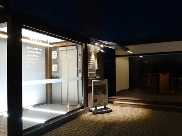 Modernes Ausstellungsgebäude mit beleuchteter Terrasse, Lamellendach und Smart-Home-Technik.