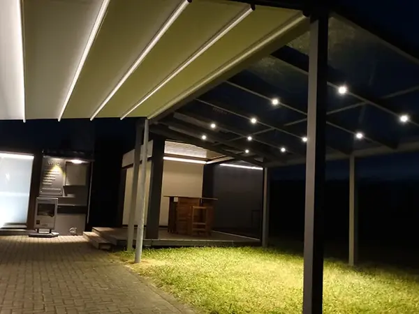 Überdachte Terrasse mit LED-Beleuchtung und moderner Markise im Garten bei Nacht.