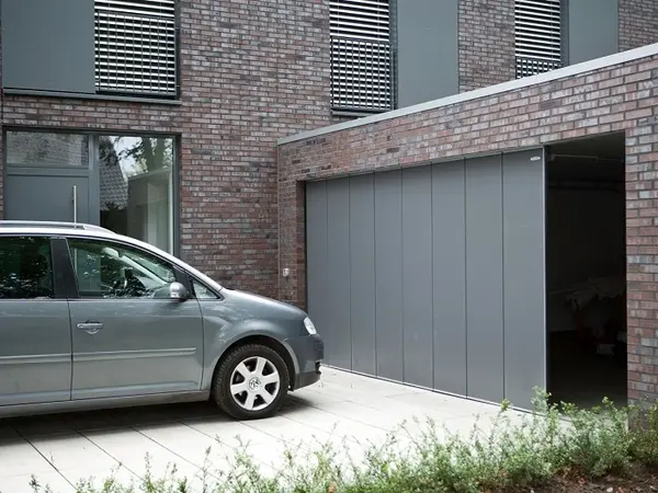 Modernes Einfamilienhaus mit grauer Garage und geparktem Auto auf gepflasterter Einfahrt.