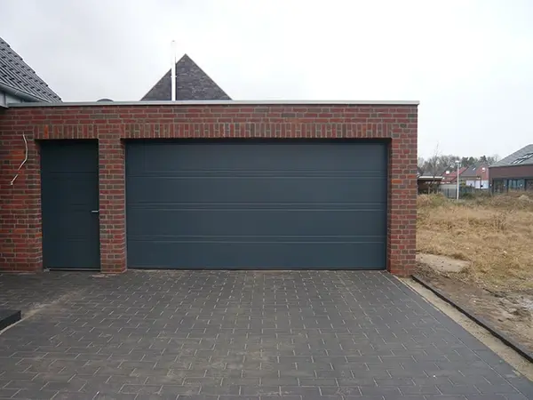 Moderne Doppelgarage mit rotem Klinker, anthrazitfarbenem Tor und gepflasterter Einfahrt.