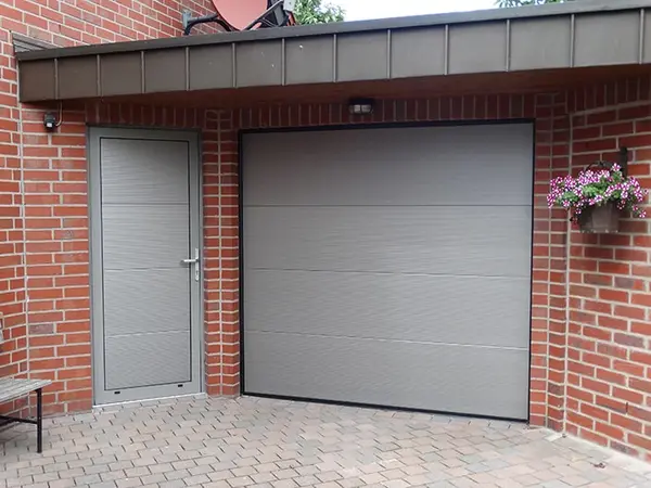 Moderne Garage mit grauem Sektionaltor und Nebentür an roter Klinkerfassade.