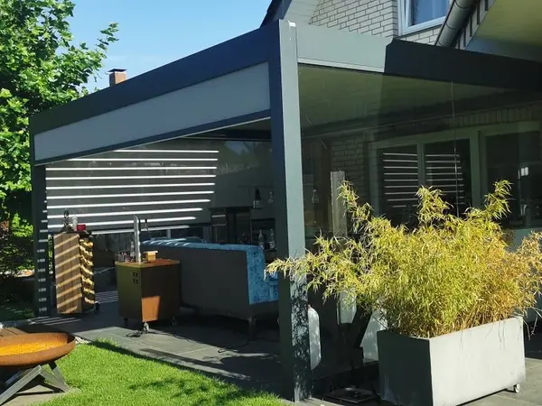 Moderne Terrassenüberdachung aus Glas und Aluminium mit gemütlicher Sitzlounge im Garten.