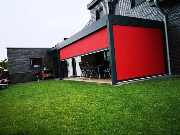 Moderne Terrasse mit rotem Sonnenschutz, Markise und Garten am Einfamilienhaus.