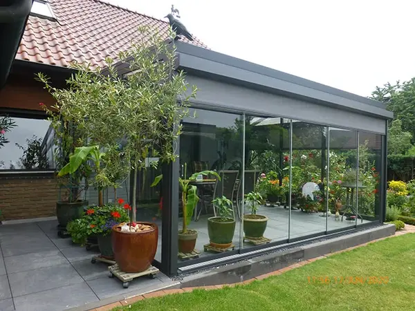 Moderner Wintergarten mit Glaswänden, vielen Pflanzen und Terrasse am Einfamilienhaus.